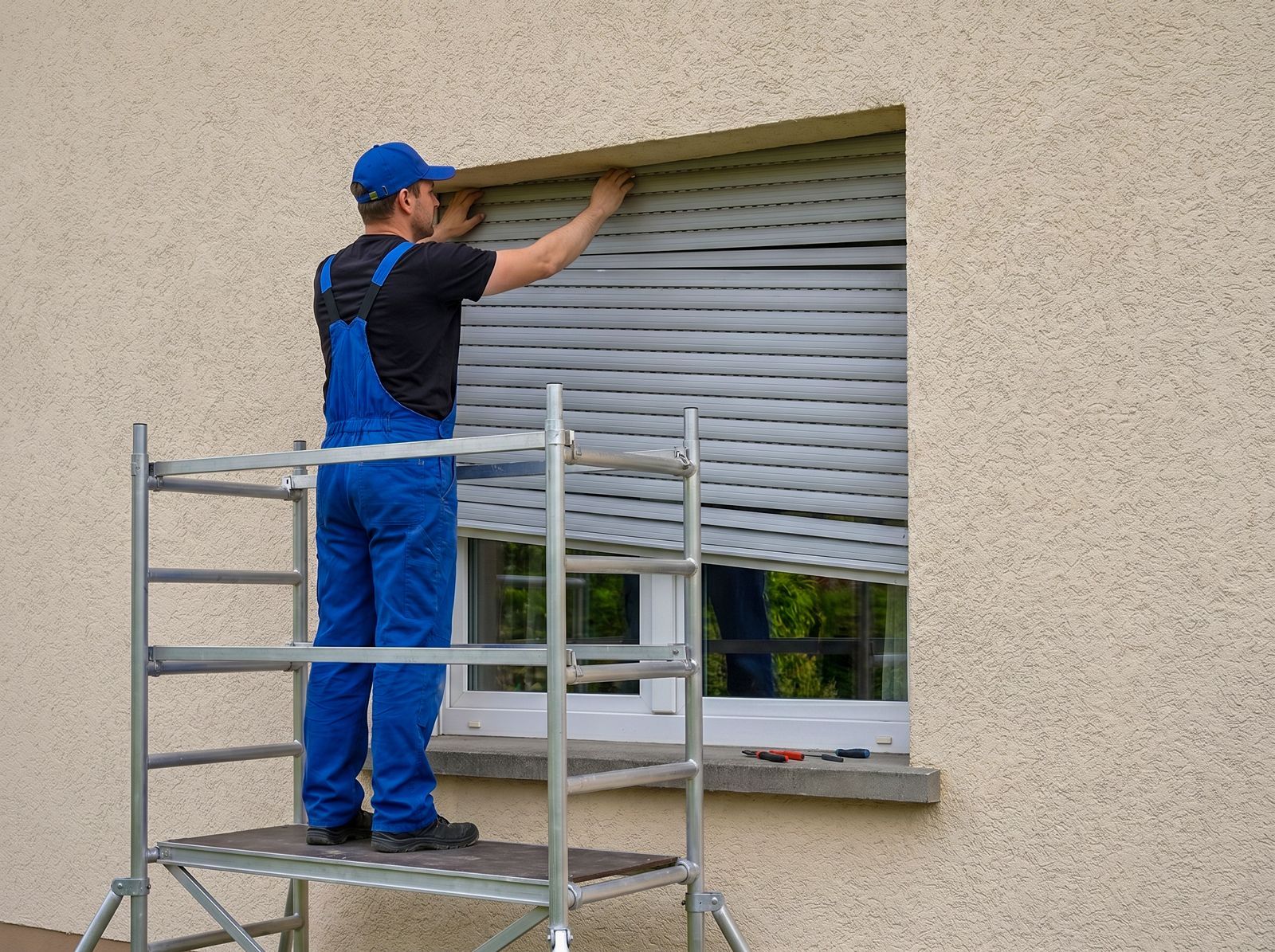 Monteur auf Arbeitsbühne repariert einen Rollladenkasten an einer Putzfassade Monteur auf Arbeitsbühne repariert einen Rollladenkasten an einer Putzfassade